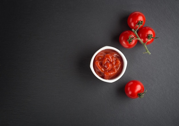 A bowl with ketchup basil and tomatoes on a black background Scoop ketchup with a spoon