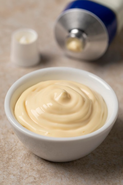 Bowl with Mayonnaise close up and a tube of mayonnaise in the background