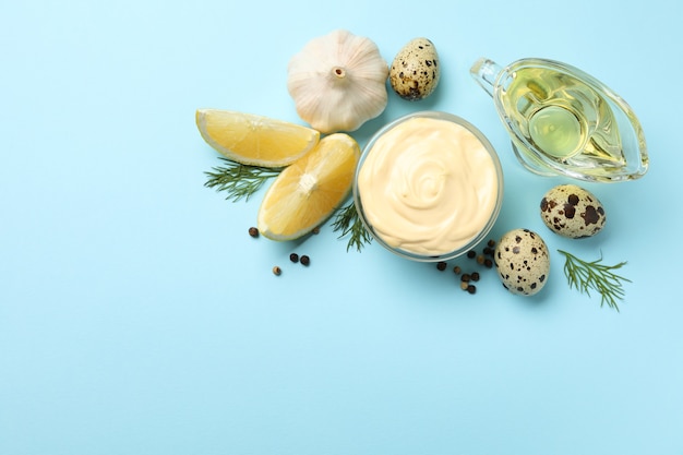 Bowl with mayonnaise and ingredients on blue background