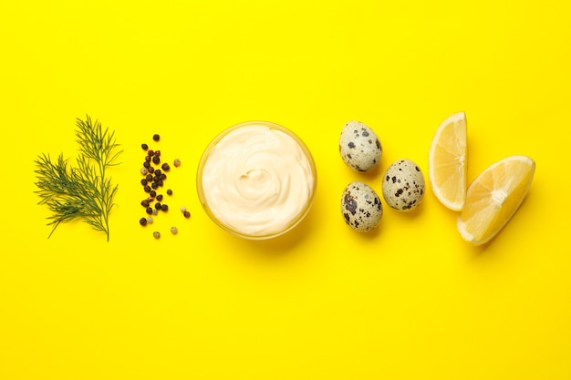 Bowl with mayonnaise and ingredients on yellow background, top view