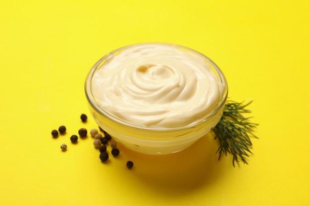 Bowl with mayonnaise, pepper and dill on yellow background