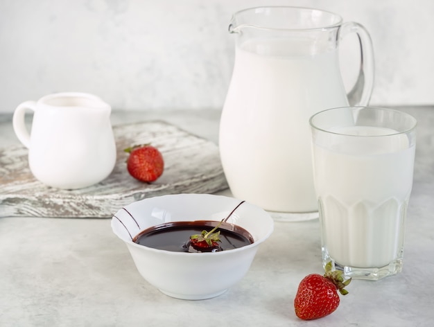 La ciotola con cioccolato fuso e fragola, bicchieri con latte, colazione estiva sfondo bianco