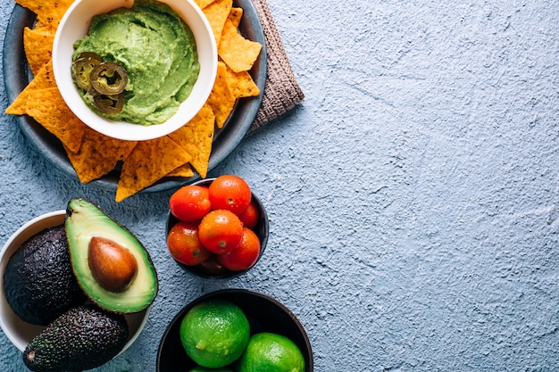 Bowl with Mexican guacamole on vintage wooden table, surrounded by tomatoes, jalapeÃÂ±os peppers, limes and avocados. Copyspace