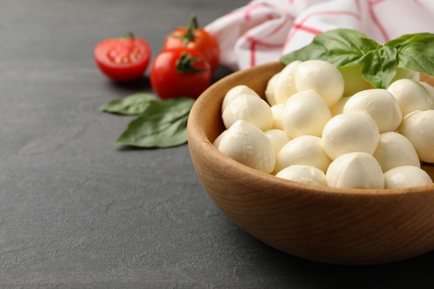 Bowl with mozzarella and basil, tomato and towel on dark textured background, space for text