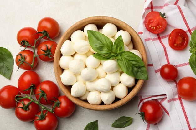 Ciotola con mozzarella e basilico, pomodoro e asciugamano su sfondo bianco con texture, vista dall'alto