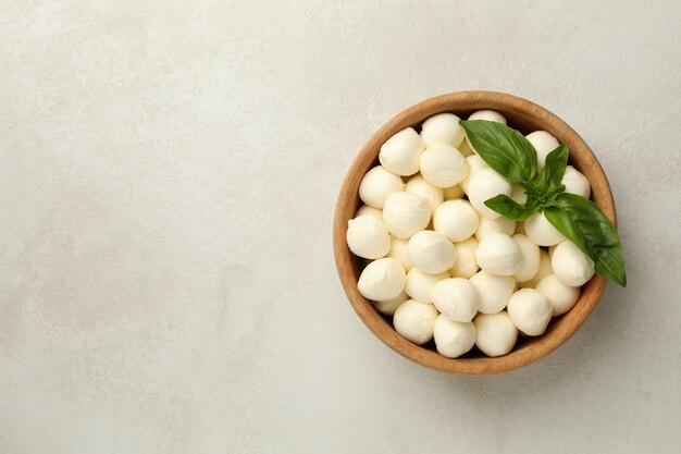 Bowl with mozzarella and basil on white textured background, space for text