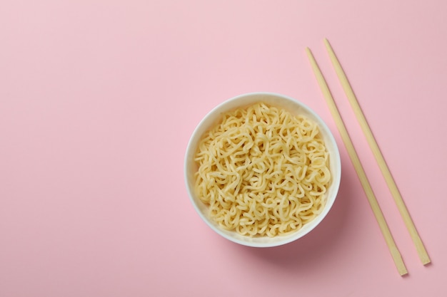 Bowl with noodles and chopsticks on pink background