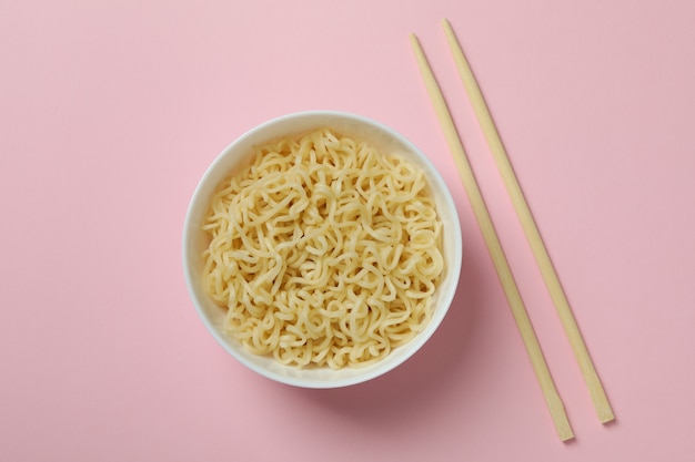 Bowl with noodles and chopsticks on pink