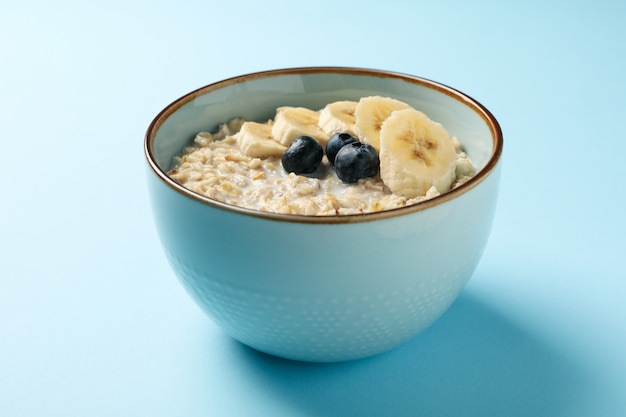Bowl with oatmeal porridge and fruits on blue