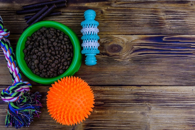 Bowl with pet food, dog toy for teeth cleaning, rope with tied\
knots and toy ball on a wooden background. top view