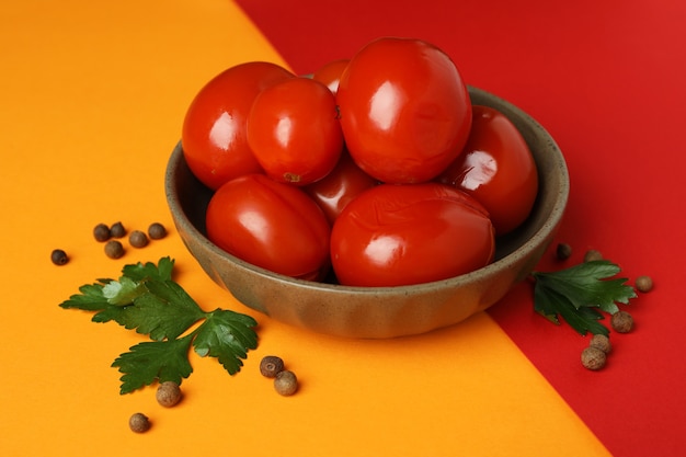 Bowl with pickled tomatoes and spices on two tone background
