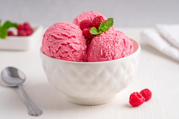 Bowl with pink scoops of sweet cold ice cream  decorated with juicy raspberries and fresh mint leaf