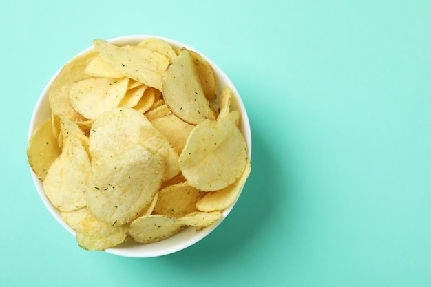 Bowl with potato chips on mint surface