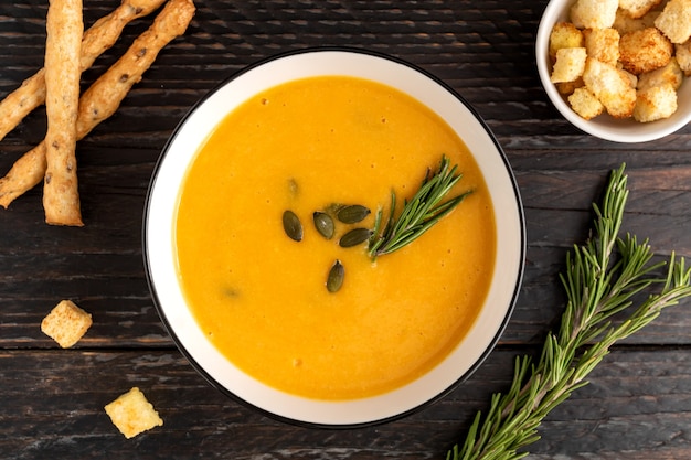 bowl with pumpkin cream soup with grossini bread sticks and resemary on dark wooden background.