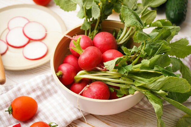 Bowl with radish and other spring vegetables on a wooden background closeup