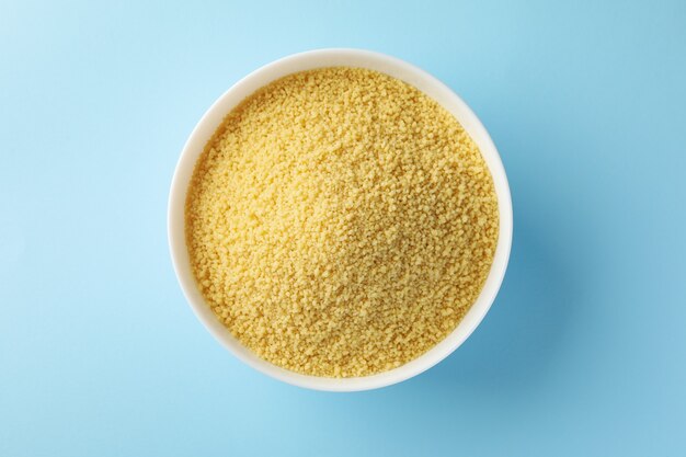 Bowl with raw couscous on blue background