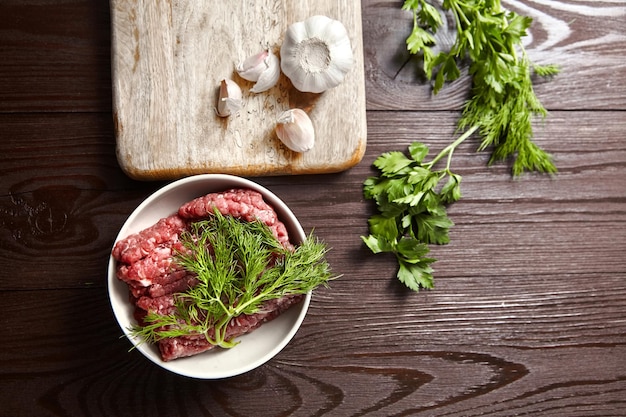 Foto ciotola con tagliere di carne macinata cruda con condimenti freschi su una vista superiore del fondo di legno