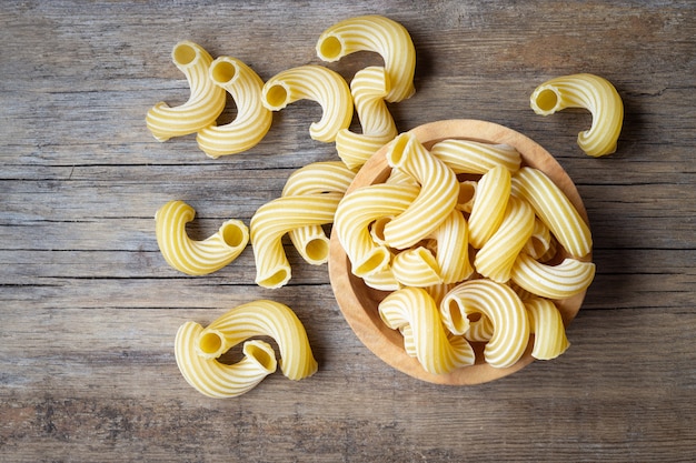 Bowl with raw pasta cavatappi on wooden background.