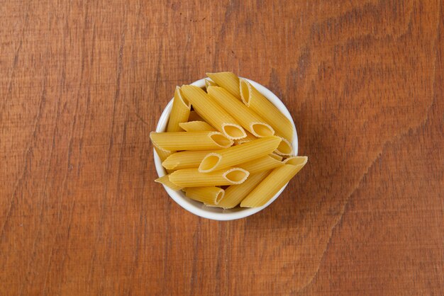 Bowl with raw pasta on wooden background