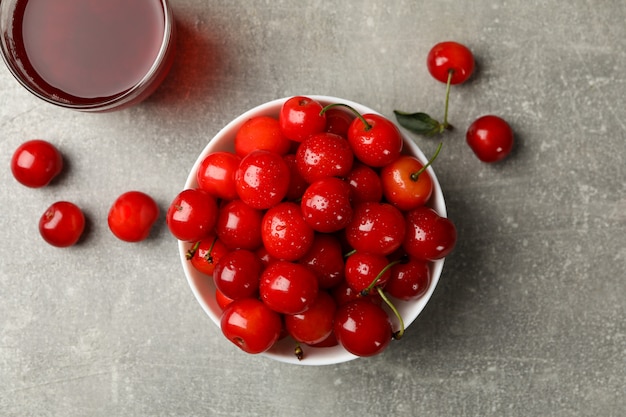 Bowl with red cherry and glass of juice on grey table