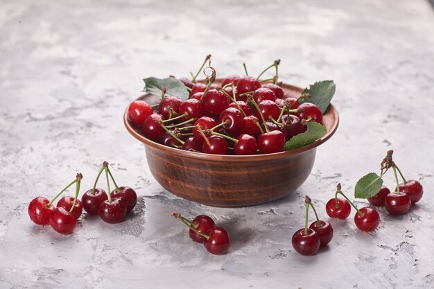 Bowl with red cherry on gray background, top view