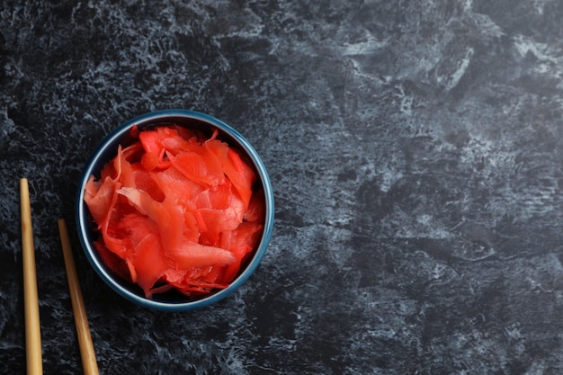 Bowl with red pickled ginger and chopsticks on black smokey