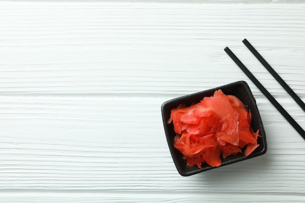 Bowl with red pickled ginger and chopsticks on white wooden surface