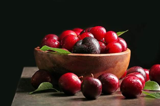 Bowl with ripe juicy plums on dark background