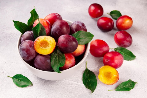 A bowl with ripe juicy plums on a gray background