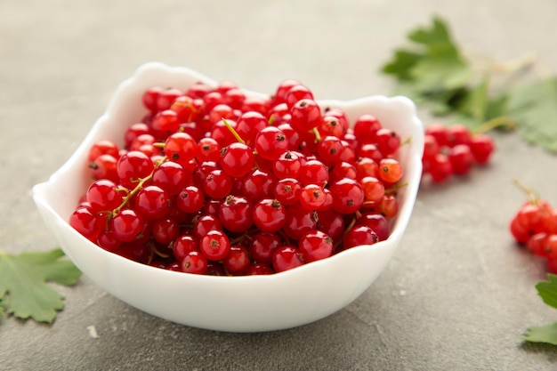 Bowl with ripe red currant on grey background