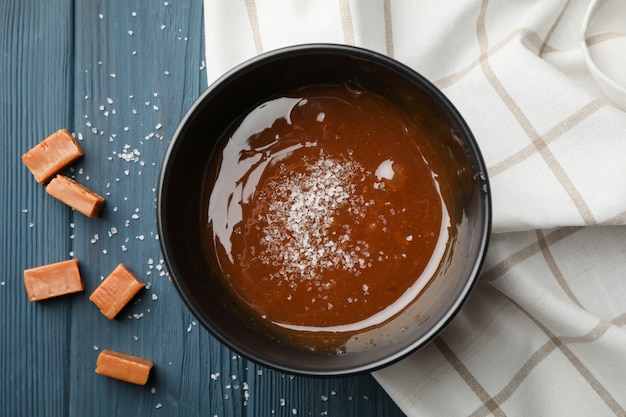 Bowl with salted caramel and candies on wooden space, top view