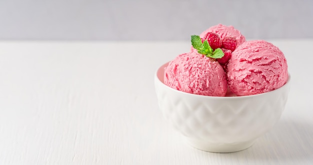 Bowl with scoops of refreshing sweet berry pink ice cream scoops with raspberries and mint leaf