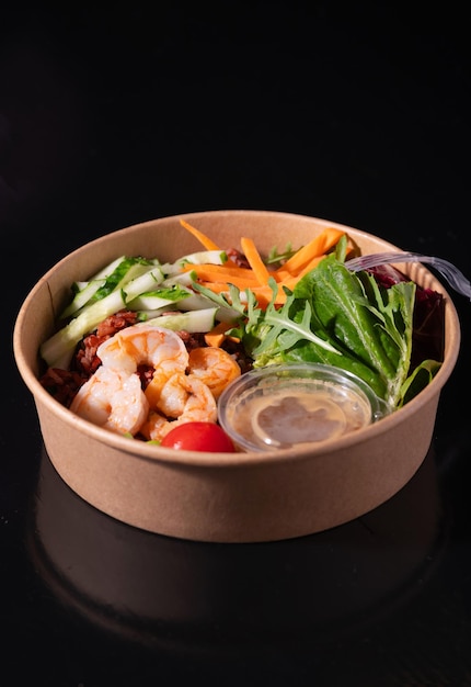 Bowl with shrimps carrots cucumbers beans and vegetables with herbs on a black background