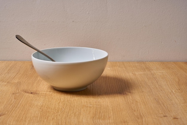 A bowl with a spoon on it sits on a wooden table.