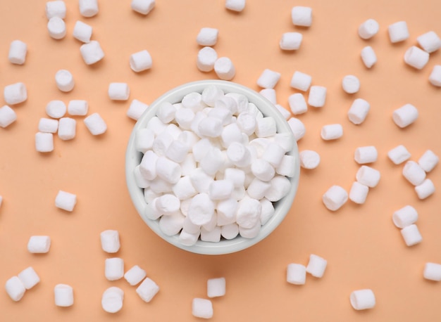 Bowl with sweet marshmallows on orange background flat lay