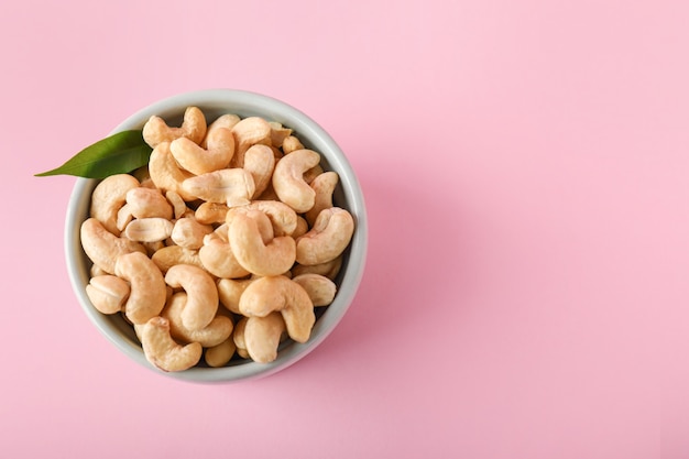 Bowl with tasty cashew nuts on color