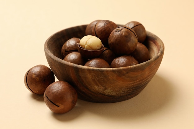 Bowl with tasty macadamia nuts on beige