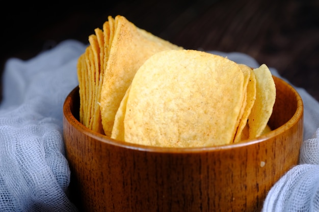 Bowl with tasty potato chips on wooden table .