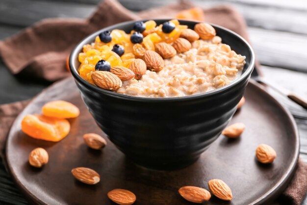 Bowl with tasty sweet oatmeal on table, closeup