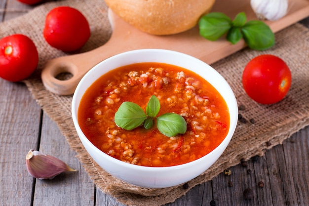 Bowl with tasty tomato soup on wooden board