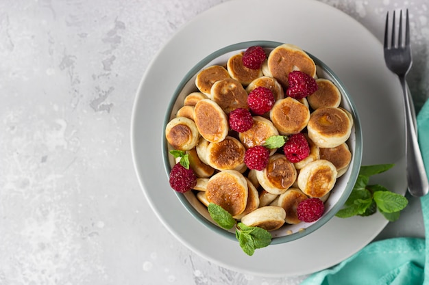 Bowl with tiny pancake cereal with raspberries, mint and jam