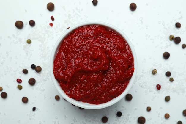 Bowl with tomato paste, pepper and salt on white surface