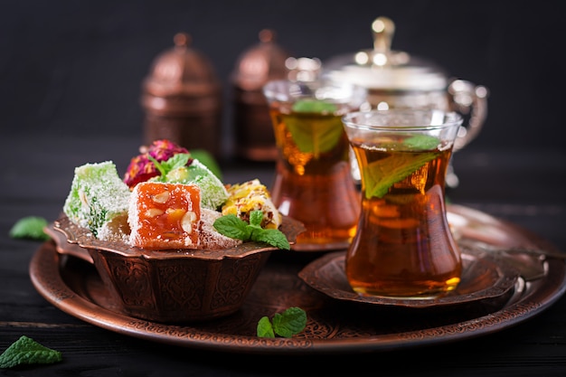 Bowl with various pieces of turkish delight lokum and black tea with mint on a dark table