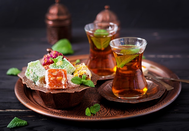 Bowl with various pieces of turkish delight lokum and black tea with mint 