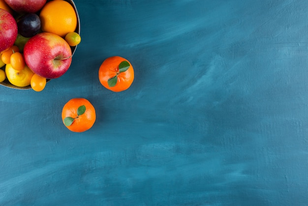 Bowl with various types of fresh juicy fruits placed on dark-blue table .