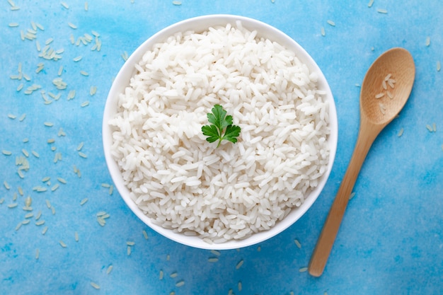 bowl with white boiled rice with green fresh parsley for delicious healthy lunch on a blue surfce