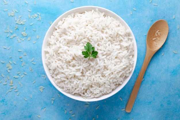 Bowl with white boiled rice with green fresh parsley for delicious healthy lunch on a blue surfce