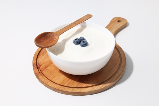 Bowl with yogurt with berries on board and wooden spoon on white background