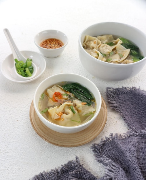 A bowl of wonton soup with a bowl of green chili.