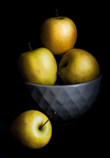 Bowl of yellow apples. On black wall.